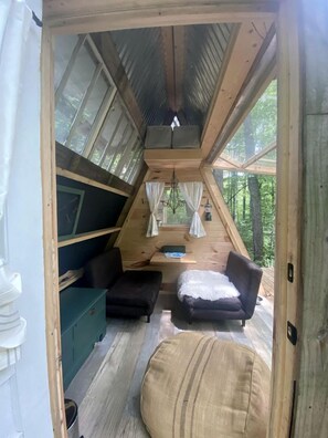 L’intérieur d’un chalet accueillant, avec un plafond en pente, des murs en bois, un canapé, un fauteuil et une petite table.