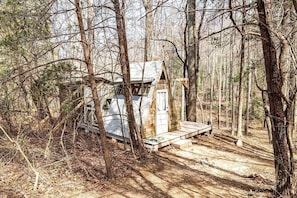Une petite cabane dans une forêt, avec une terrasse en bois et une porte.