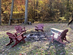 A campsite with a fire pit, wooden chairs, and a picnic table surrounded by trees. - Amazing Tiny House Rental for Unique Romantic Getaways in Tennessee (Grandview)
