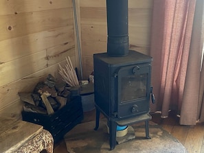 A wood-burning stove, a stack of firewood, and a window with curtains. - Amazing Tiny House Rental for Unique Romantic Getaways in Tennessee (Grandview)