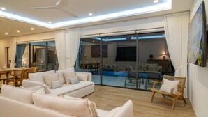 Un salon moderne doté d’un grand canapé, d’un coin repas et d’une porte vitrée donnant sur un balcon avec une piscine.