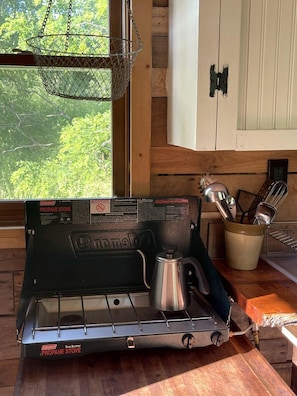 Une cuisinière au propane avec une casserole en métal, un panier suspendu en fil de fer et des armoires en bois.