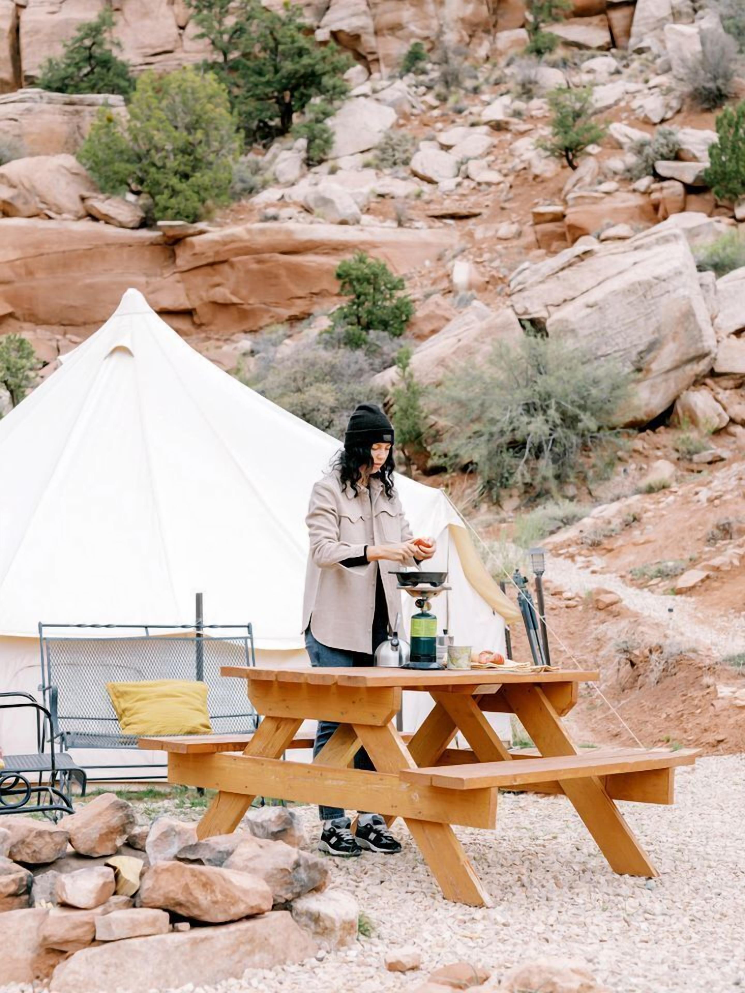 Une tente, une table de pique-nique et une personne équipée pour le camping, le tout dans un environnement extérieur rocheux.