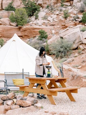 Une tente, une table de pique-nique et une personne équipée pour le camping, le tout dans un environnement extérieur rocheux.