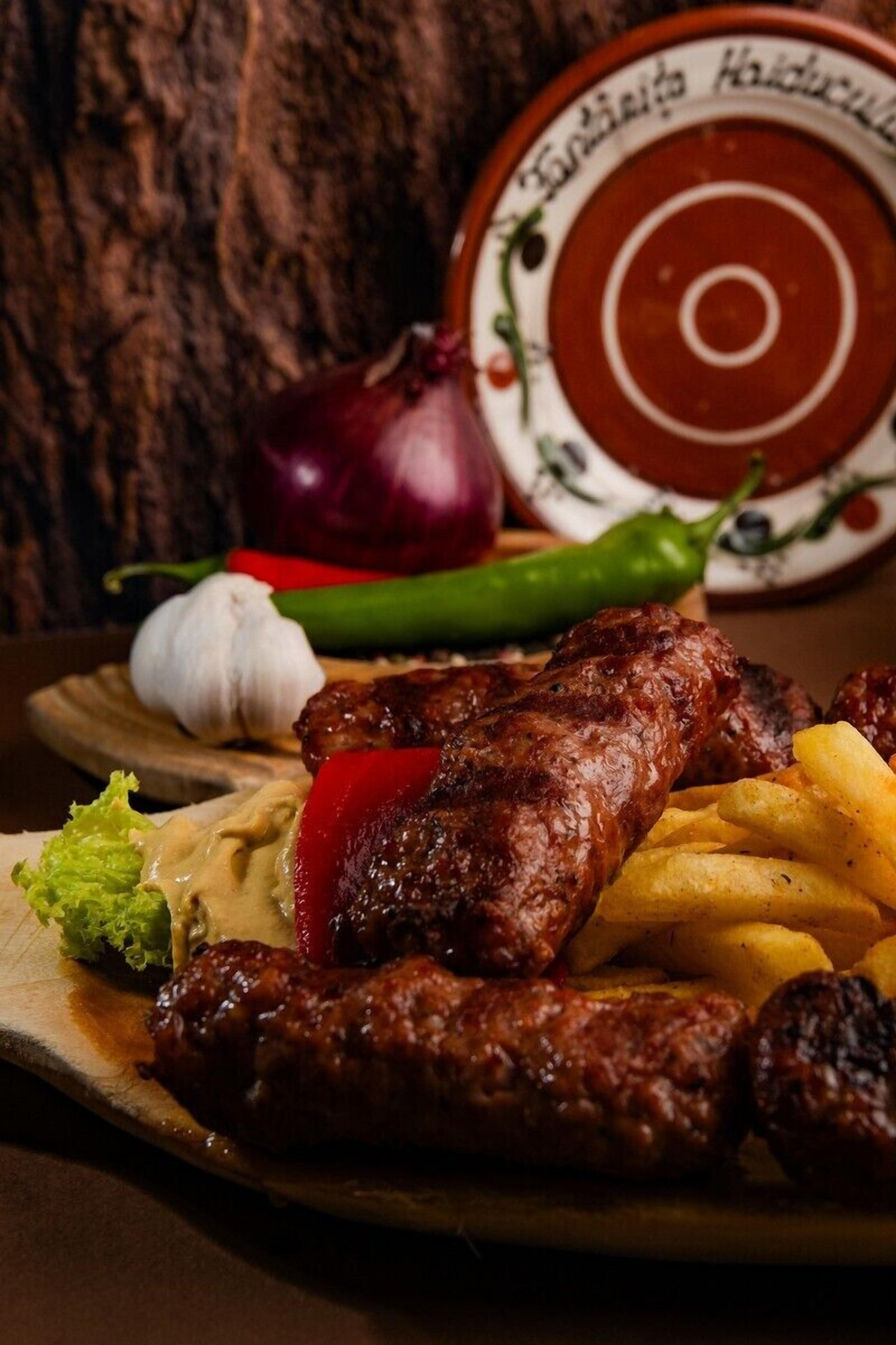 Um prato com linguiça grelhada, batatas fritas e uma salada acompanhada de cebola roxa, alho e um pimentão verde.
