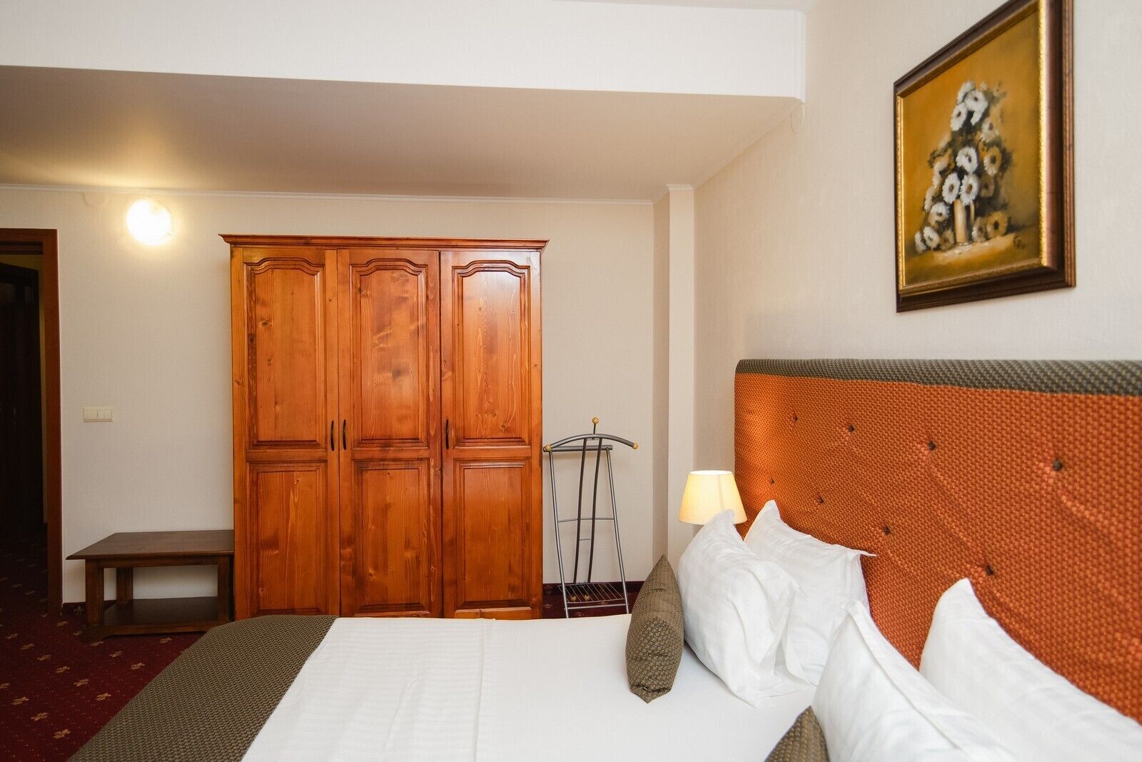 Une chambre d’hôtel avec une grande armoire en bois, un lit avec une literie blanche, une lampe et un tableau au mur.