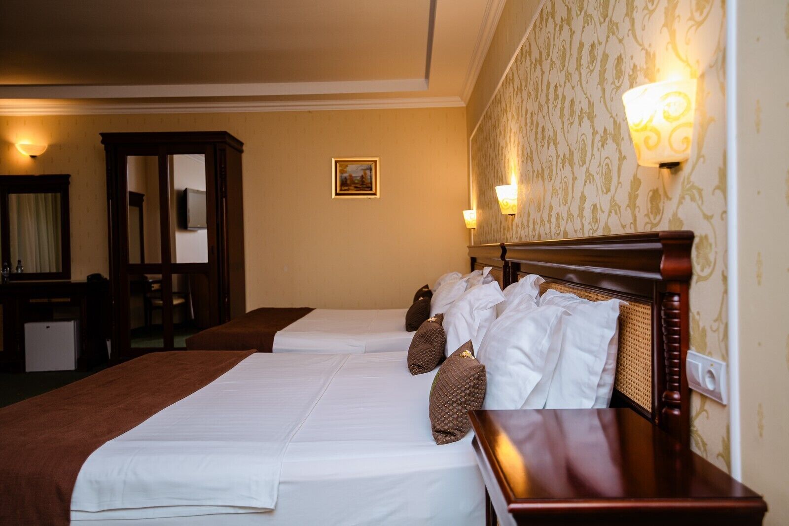 A hotel room with two beds, a wooden headboard, a desk, and a mirror.