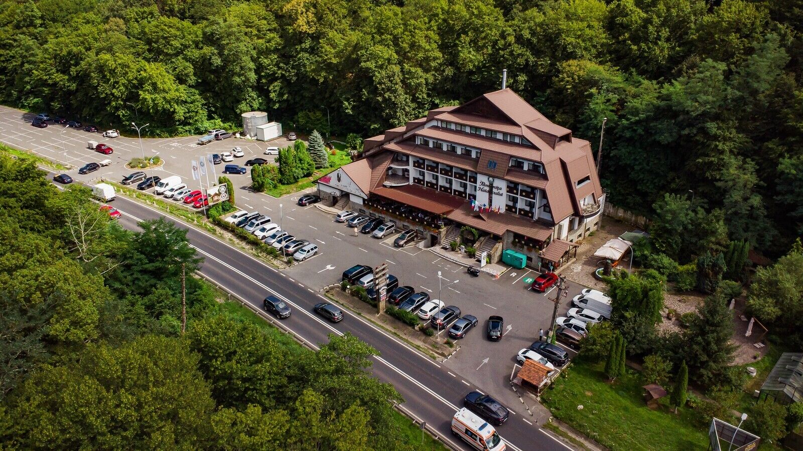 An aerial view of a hotel with a parking lot, surrounded by dense greenery.