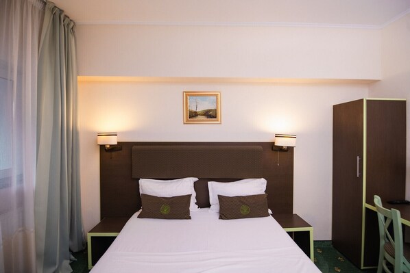 Ein Hotelzimmer mit einem großen Bett, zwei Nachttischlampen, einem Kleiderschrank und einem gerahmten Bild an der Wand.