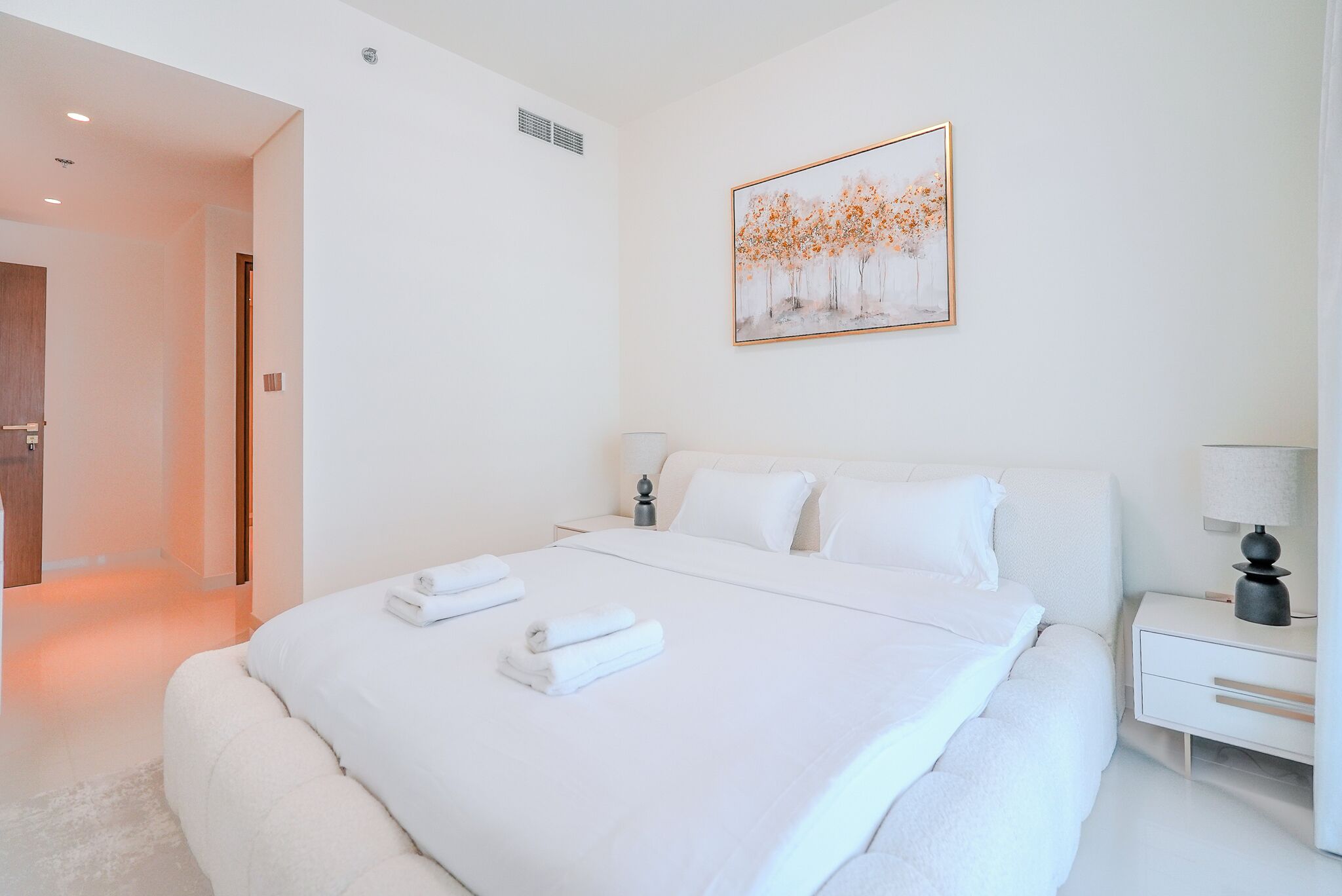 Une chambre à coucher moderne avec un grand lit, du linge de lit blanc, une table de chevet avec une lampe et un tableau au mur.