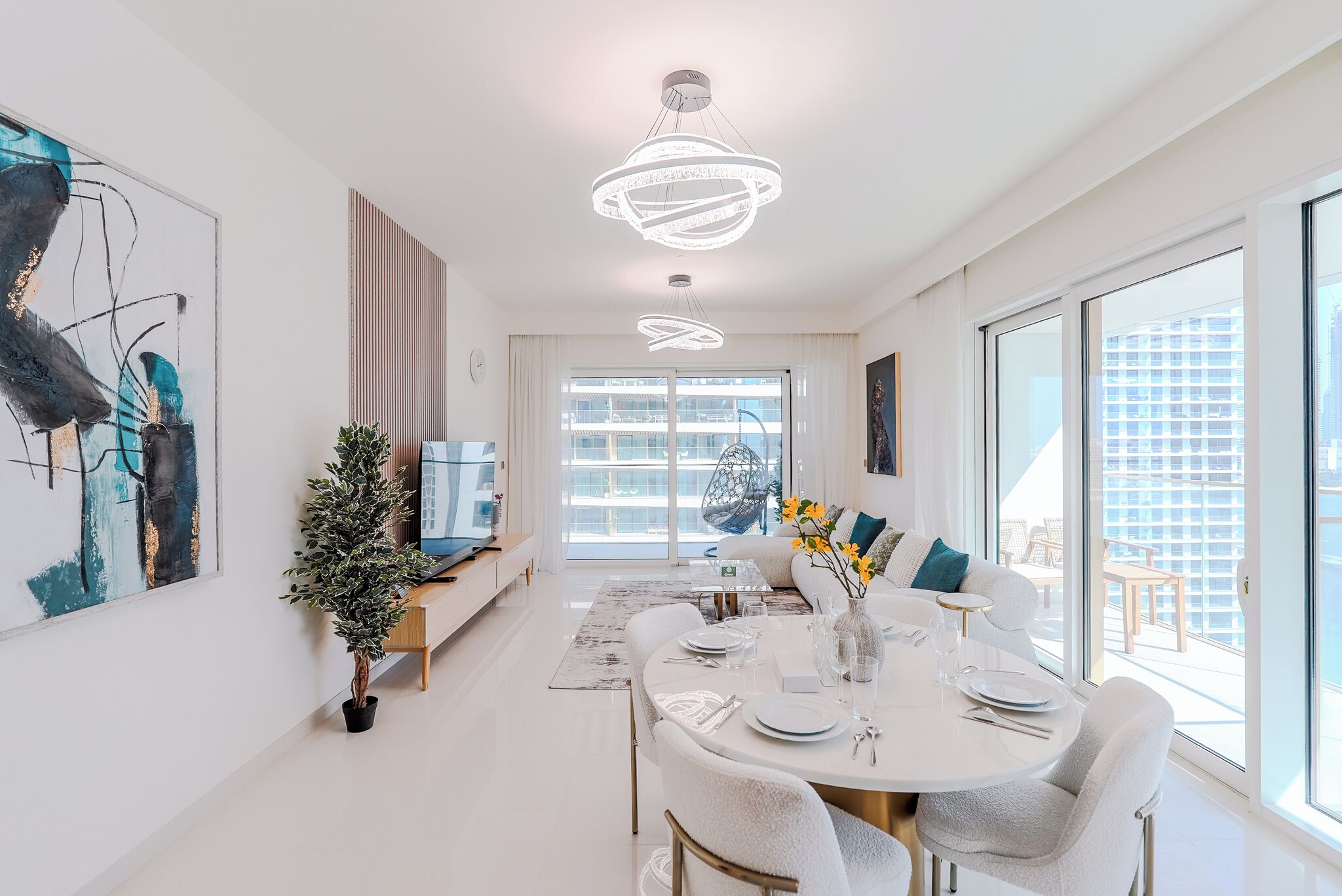 A modern dining area with a round table set for four, a potted plant, and a large window offering a view of the city.