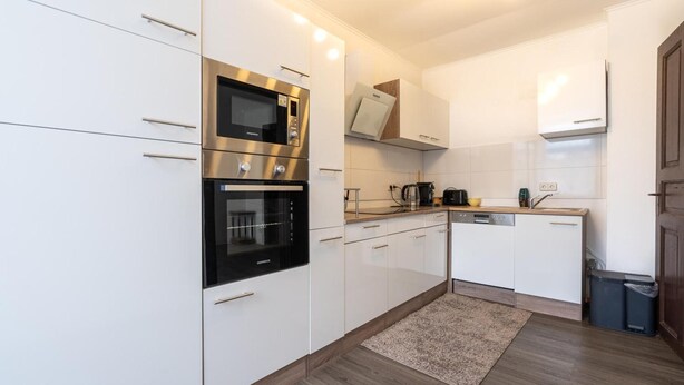 A modern kitchen with white cabinetry, stainless steel appliances, and a wooden floor.