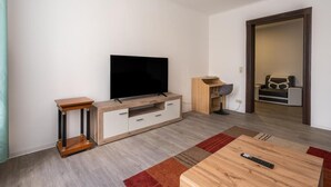 A modern living room with a flat-screen TV, wooden furniture, a coffee table, and a sofa.