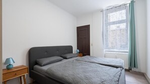 A bedroom with a bed, bedside tables, a window with curtains, and a door.