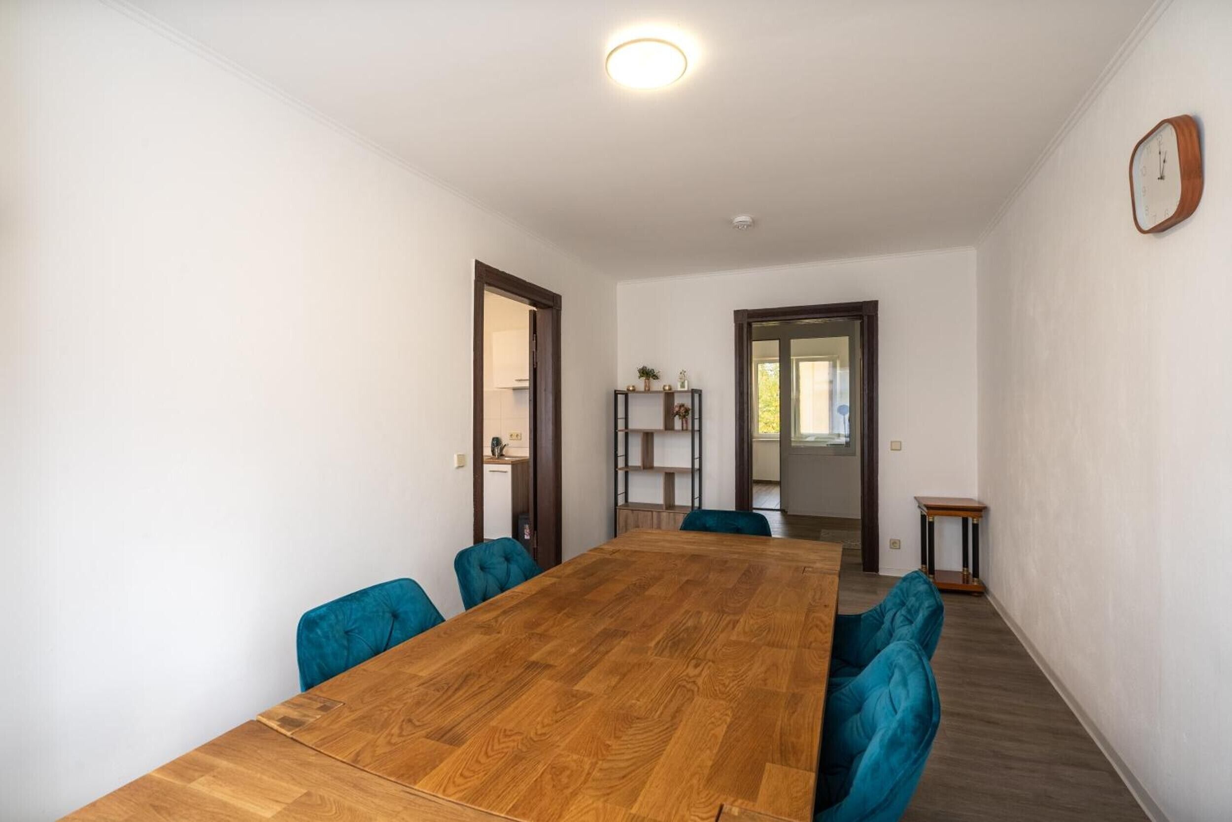 Una sala de conferències amb taula de fusta i cadires blaves, parets blanques i un rellotge a la paret.