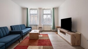 A living room with a sofa, coffee table, TV, and windows with curtains.