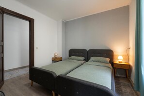 Ein Zimmer mit zwei Betten, einer Tür, einem Nachttisch mit Lampe und einer Wandleuchte.