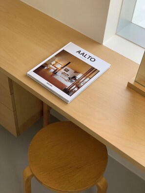A magazine titled "Aalto" on a wooden desk with a round wooden stool.