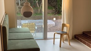 A modern living room with a green sofa, a wooden chair, and a table with books. - Villa Tuuli (Jeju City)