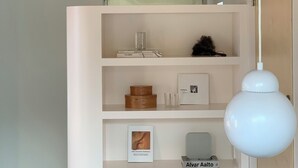 A room with a white shelving unit displaying books, a framed picture, and a small Alvar Aalto table lamp. - Villa Tuuli (Jeju City)