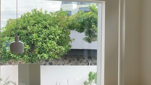 A bedroom with a large window, a bedside table, a chair, and a hanging light fixture. - Villa Tuuli (Jeju City)