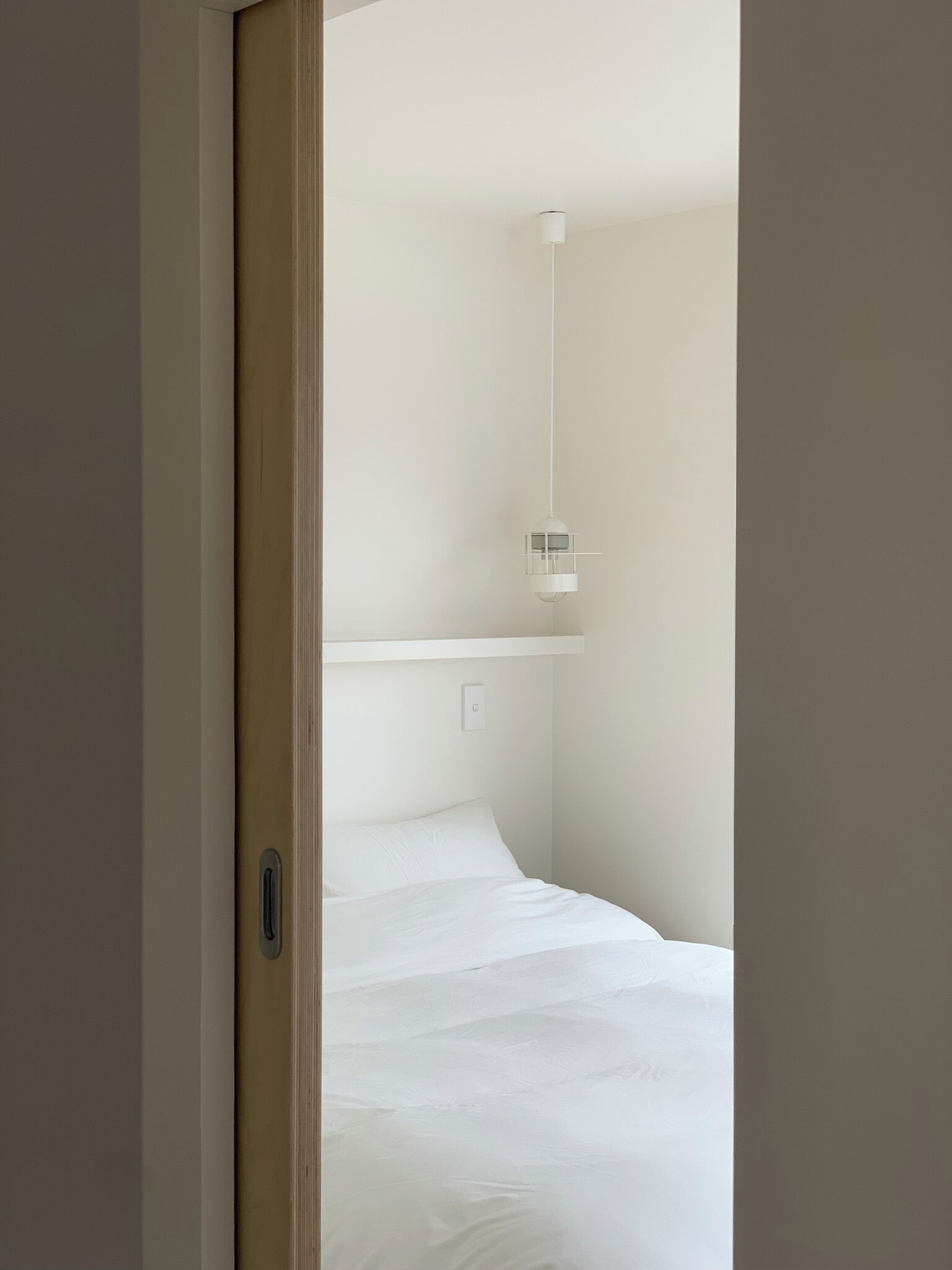 A bedroom with a bed, a hanging light fixture, and a door.