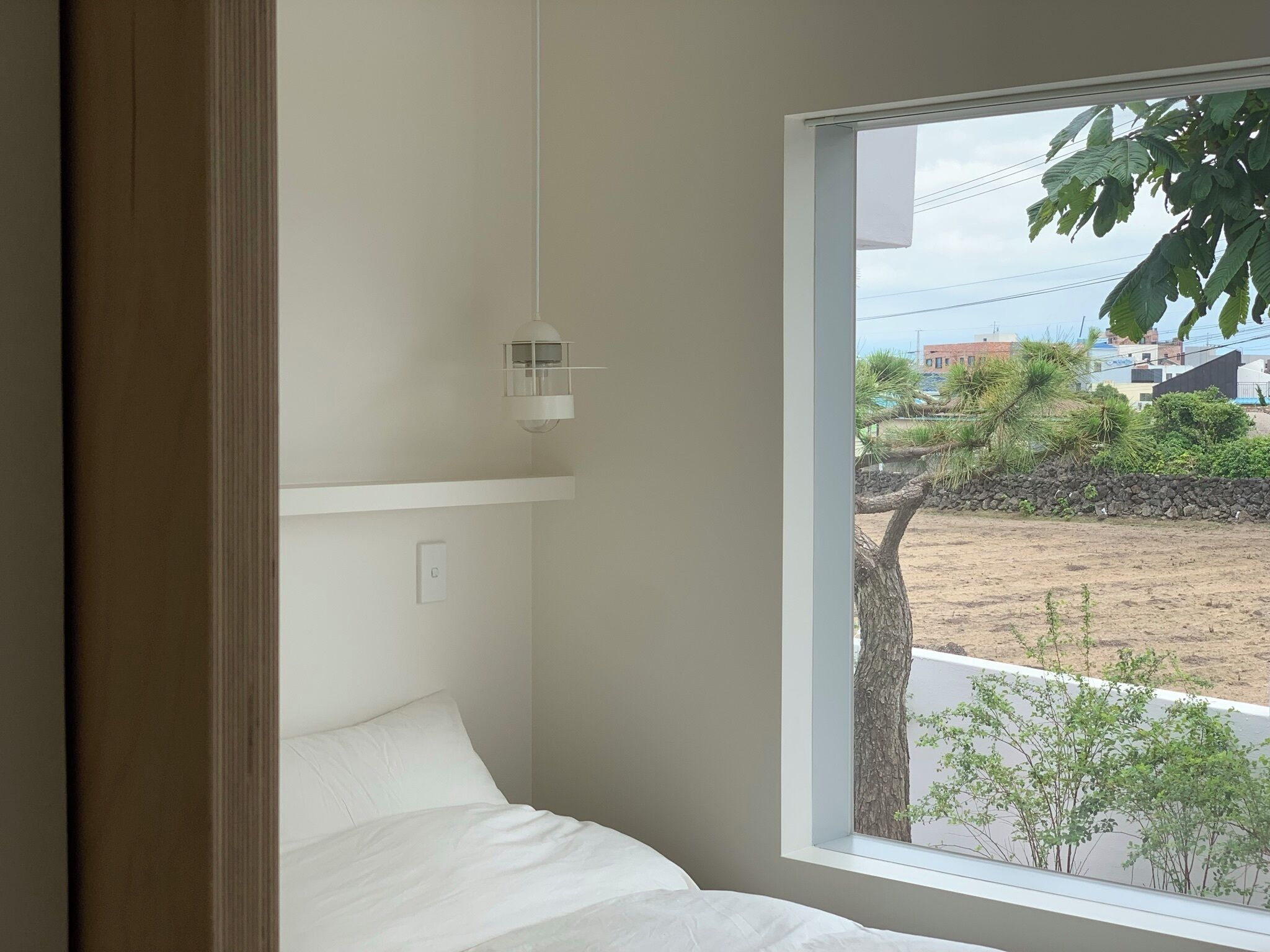 A bedroom with a large window, a bedside table, and a hanging light fixture.