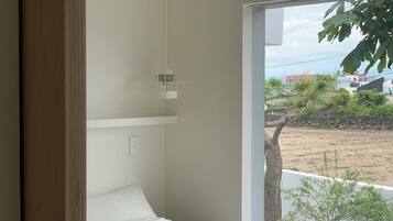 A bedroom with a large window, a bedside table, and a hanging light fixture.