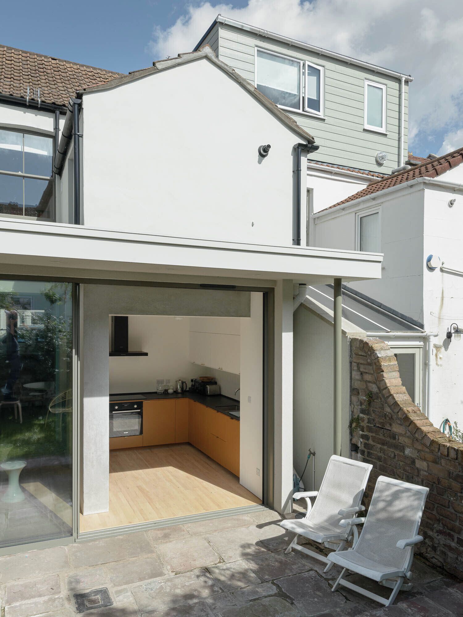 A modern house with a glass-enclosed patio, a kitchen, and two white lounge chairs.