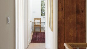 A hallway with wooden flooring, white walls, and a wooden door. There is a chair with a lamp in the distance. - Beautiful 3 Bedroom Home in Bristol (Bristol)