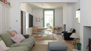 A living room with a green sofa, a grey ottoman, a dining table with chairs, and a fireplace. - Beautiful 3 Bedroom Home in Bristol (Bristol)