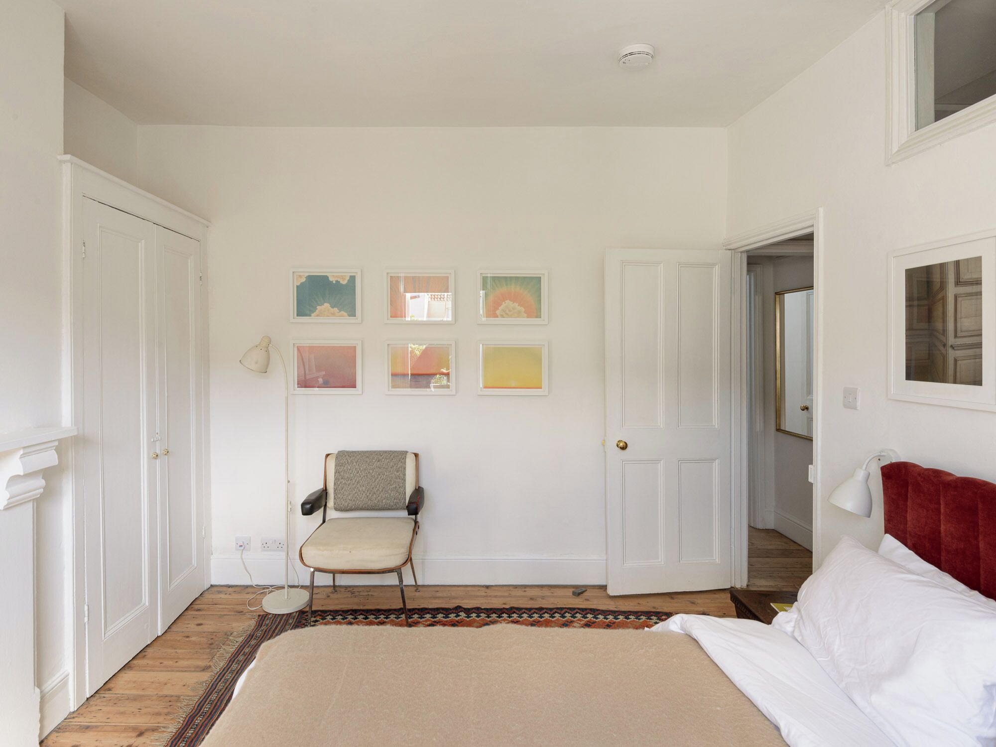 Quarto com cama, uma cadeira, tapete e parede com quadros.