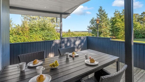 An outdoor patio with a wooden table set for breakfast, surrounded by wicker chairs, overlooking a scenic landscape. - "Leani" - 150m from the sea by Interhome (Ørsted)
