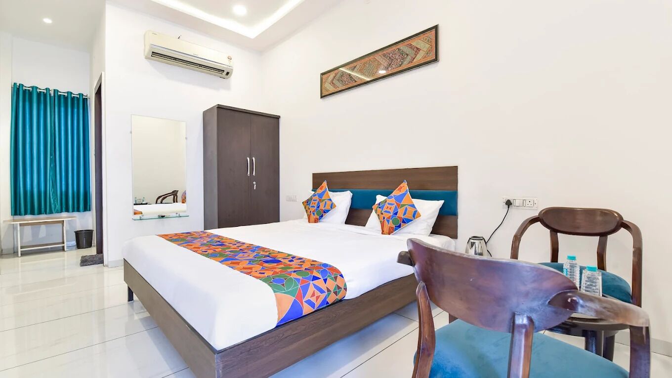 A hotel room with a large bed, a wooden headboard, a desk with a chair, a wardrobe, and a bathroom with a shower curtain.
