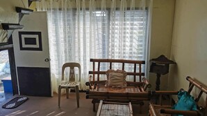 A room with a bed, a chair, a table, and a window with curtains. - Charming 1-bedroom apartment house in Pinamalayan,Oriental Mindoro (Mimaropa)