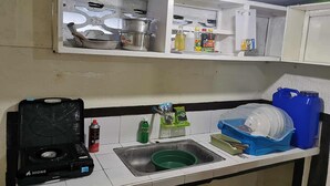 A kitchen with a gas stove, sink, and various kitchen items like a water dispenser, dish rack, and storage containers. - Charming 1-bedroom apartment house in Pinamalayan,Oriental Mindoro (Mimaropa)