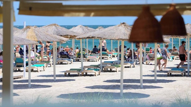 A beach with sun umbrellas and lounge chairs, people relaxing, and a clear view of the ocean. - Stefan Building Mamaia Nord (Mamaia-Sat)