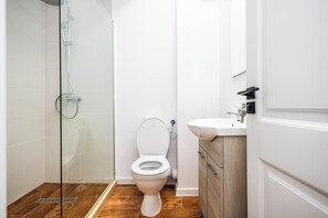 A modern bathroom with a glass-enclosed shower, a white toilet, and a wooden vanity with a sink. - Stefan Building Mamaia Nord (Mamaia-Sat)