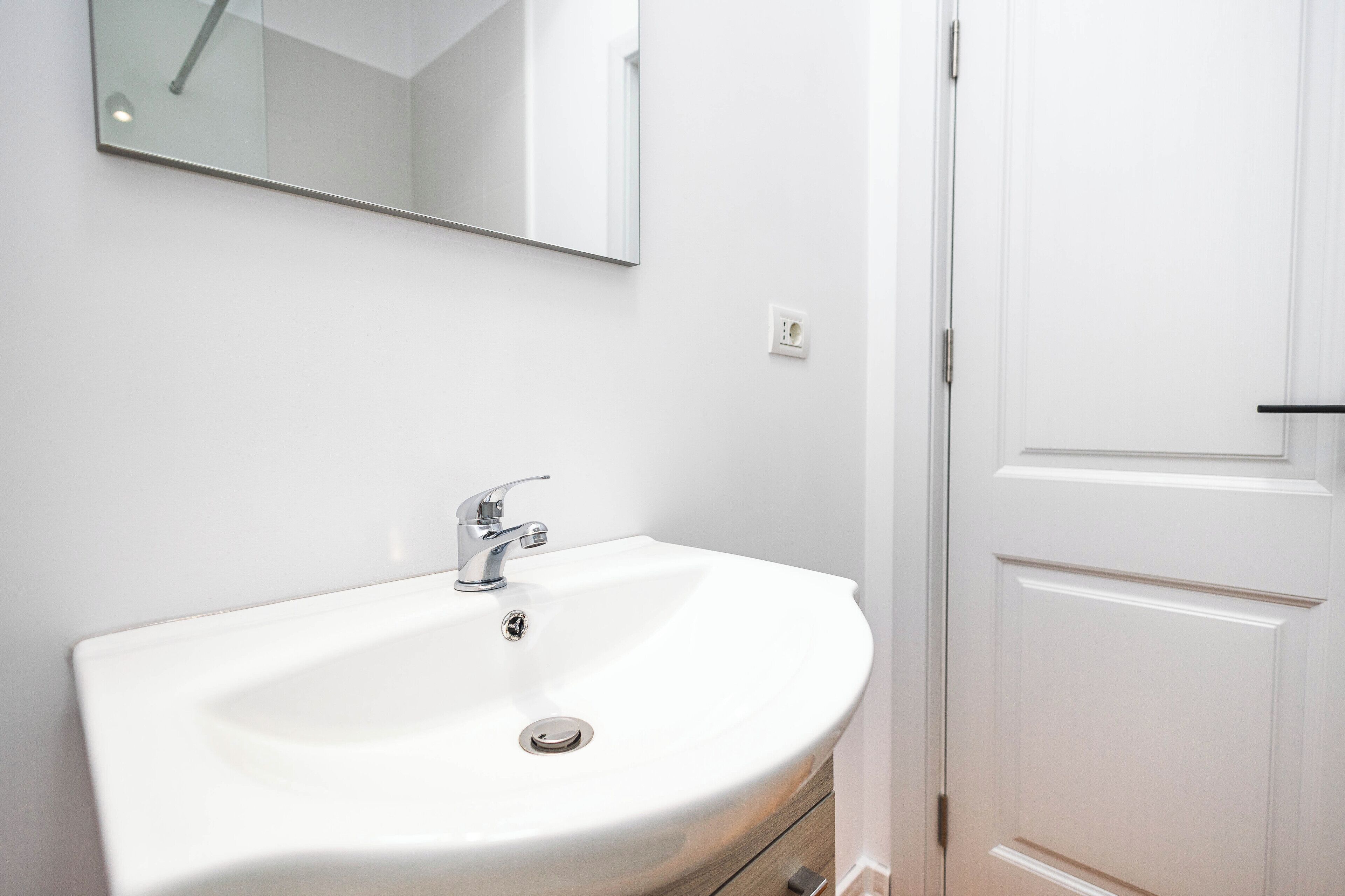 A white bathroom with a sink, a mirror, and a door.
