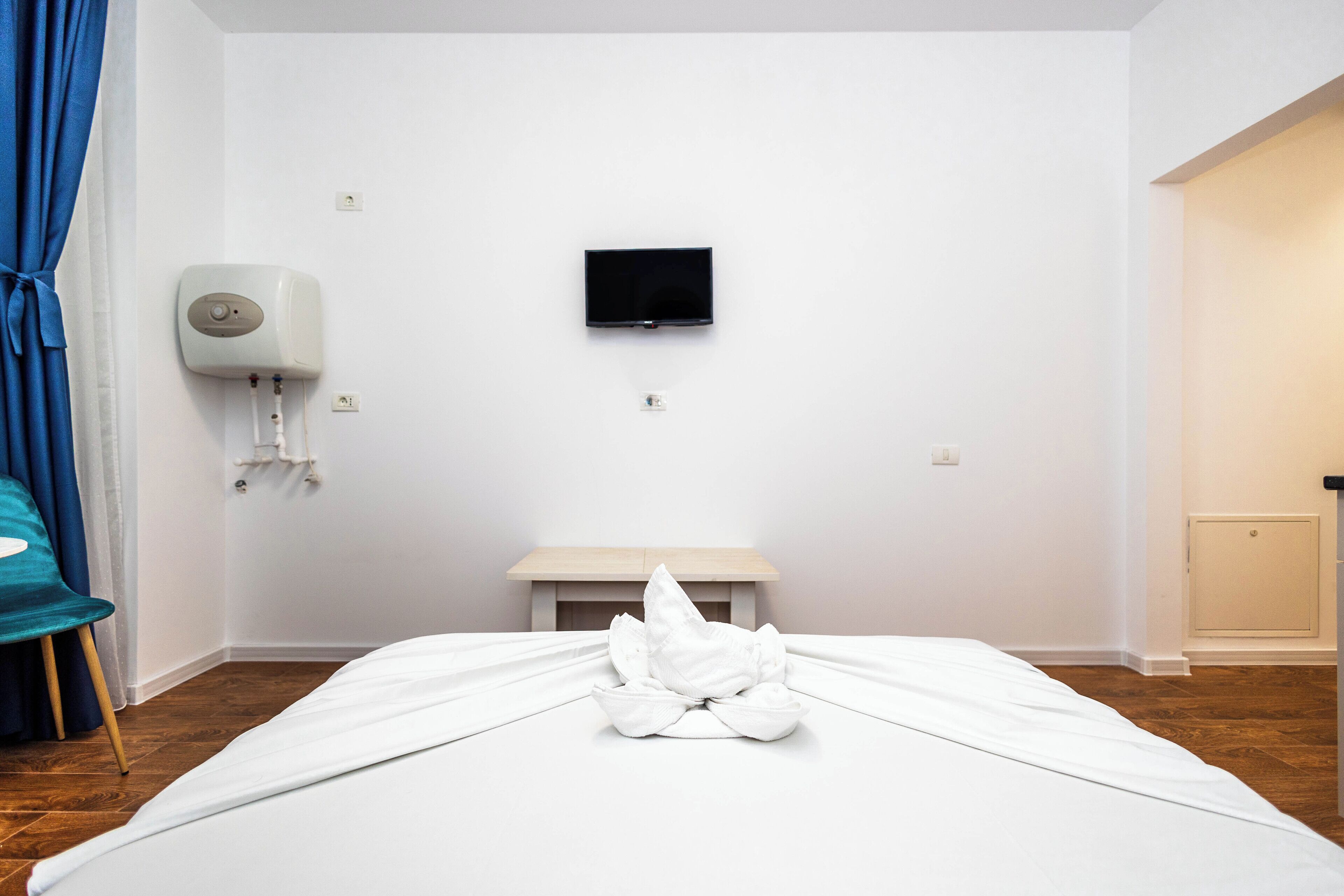 A hotel room with a bed, a TV mounted on the wall, a small table, and a towel on the bed.