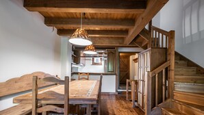 Een rustiek interieur met een houten eettafel en banken, een trap en een keukenhoek.