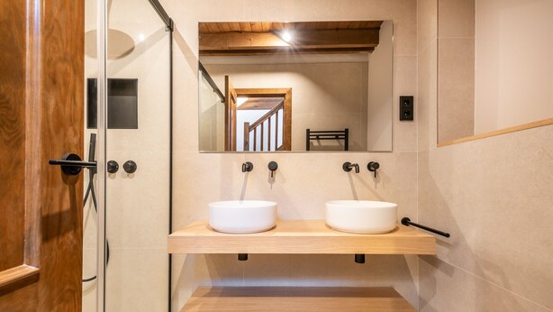 Een badkamer met twee witte wastafels, een houten plank, een spiegel en een douche.