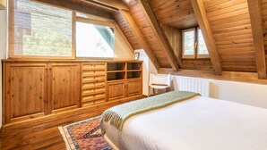 Een slaapkamer met een schuine kap, houten meubels, een bed en grote ramen.