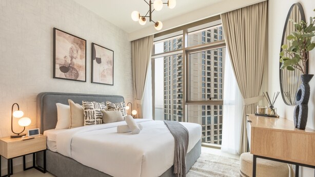 Una camera d'hotel moderna con un letto grande, lampade ai comodini, una scrivania e vista sulla città attraverso ampie finestre.