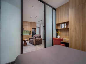 Ein modernes Schlafzimmer mit Bett, Schreibtisch, Stuhl und einer kleinen Küche im Hintergrund.