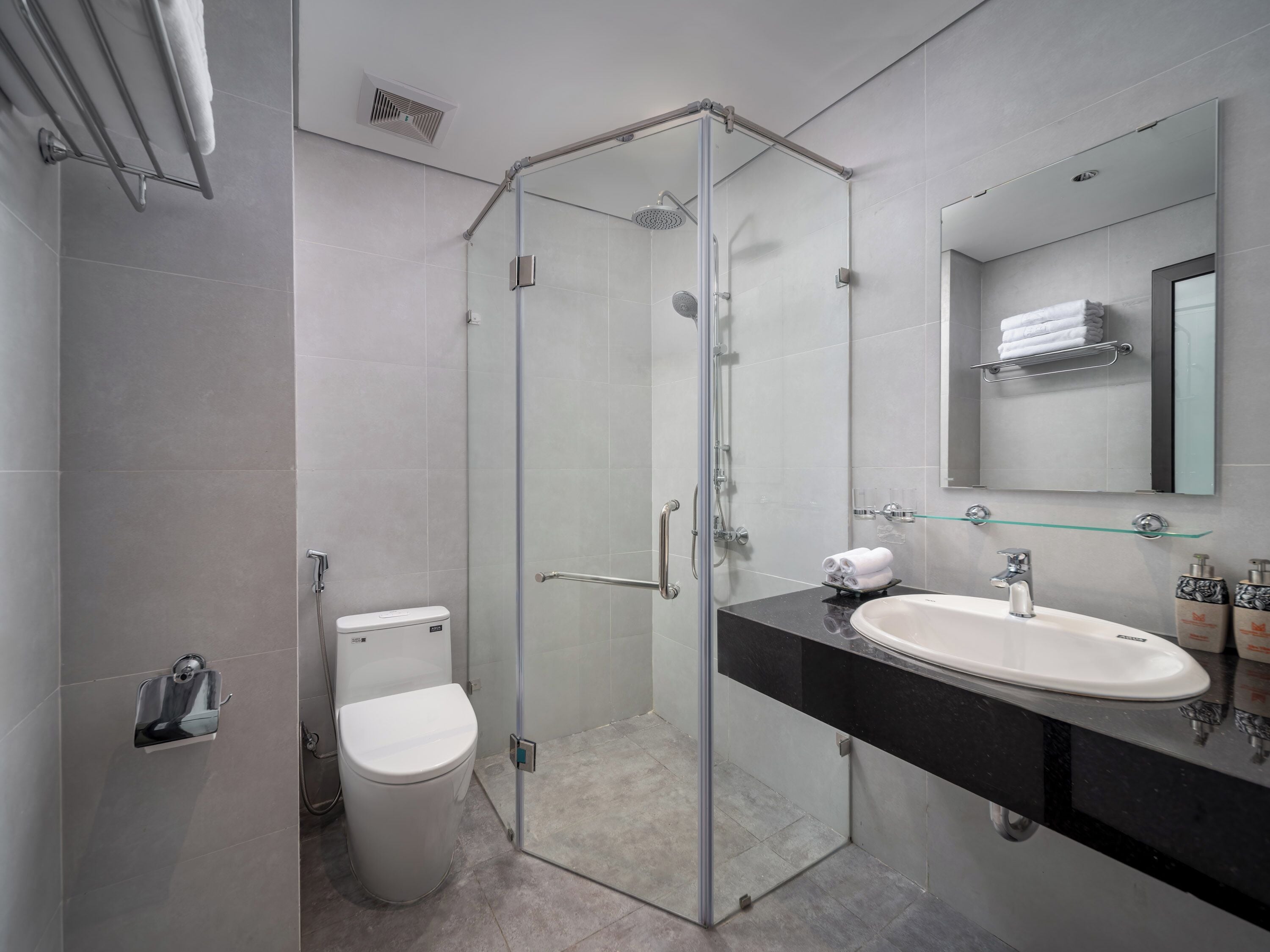 Ein modernes Badezimmer mit einer Duschkabine, einer weißen Toilette und einer schwarzen Ablage mit Waschbecken und Spiegel.