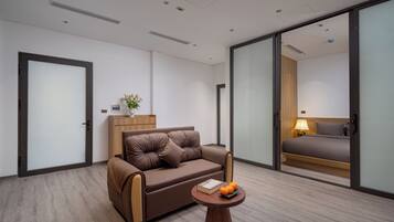 Ein modernes Hotelzimmer mit einer braunen Ledersofa, einem Holztisch mit einem Buch und Orangen sowie einem Bett mit einem Holz-Kopfteil.
