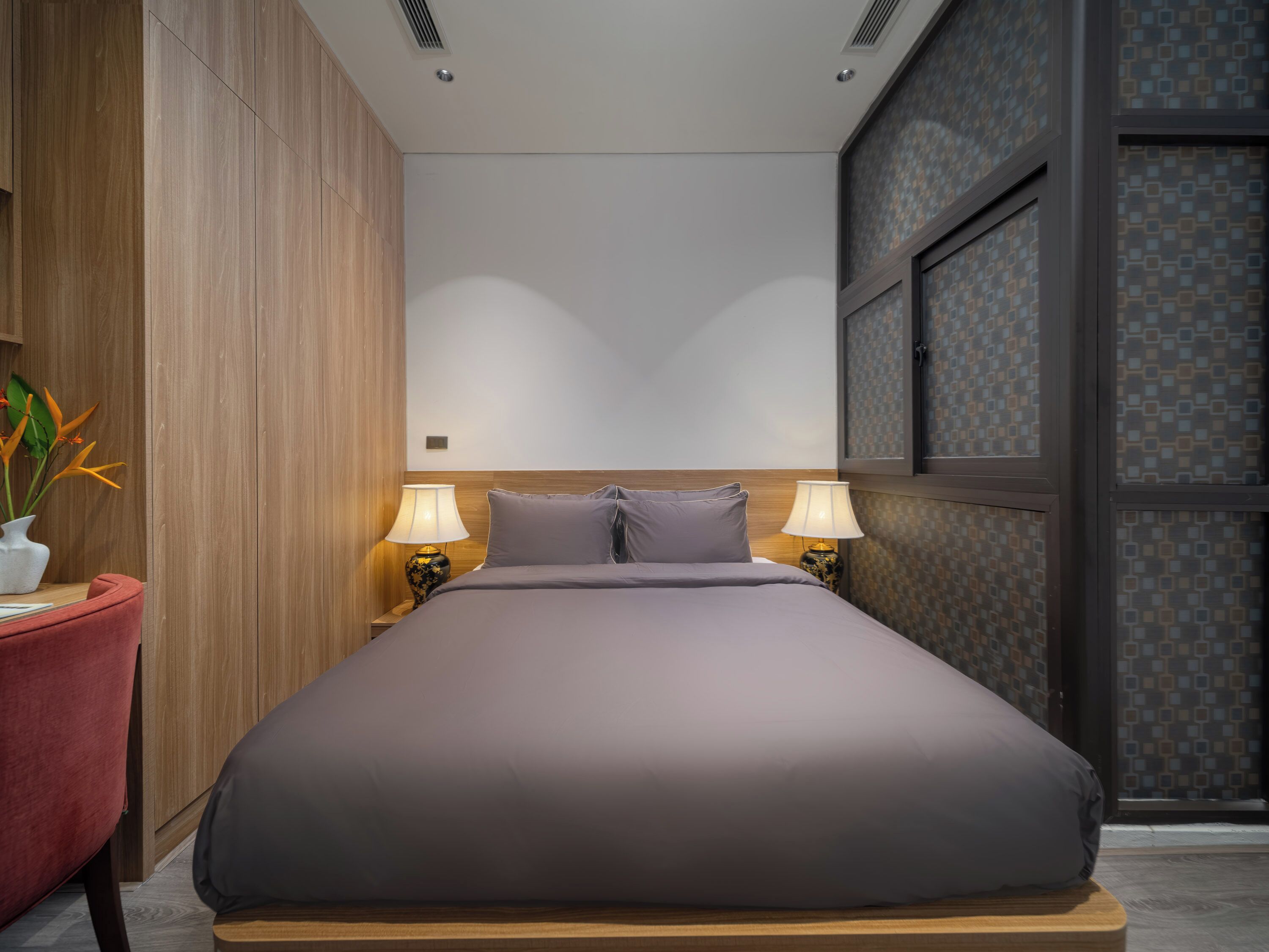 Una habitación de hotel moderna con una cama grande, dos lámparas de noche, un cabecero de madera y una ventana con cortinas estampadas.
