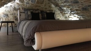 Une chambre avec un plafond en pierre, un lit recouvert d’une couverture à rayures et une petite table.