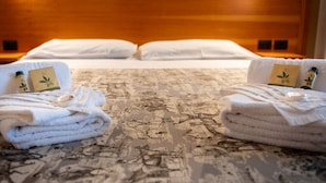 A hotel room with a bed, two towels with green leaf designs, and a bottle of lotion on the bed. - Tenuta dell'Argento - Room 4 by Rentbeat  (Civitavecchia)